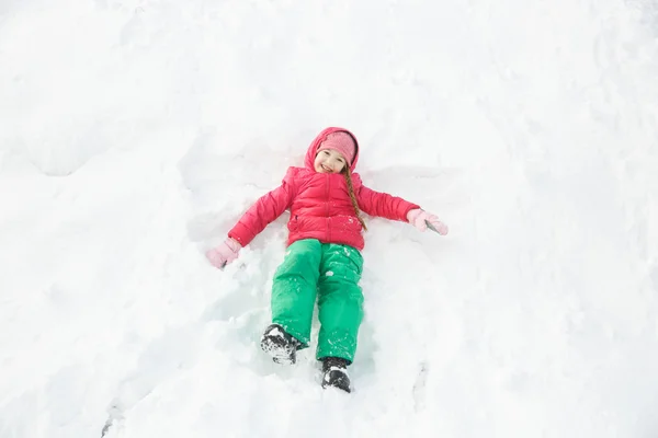 Грайлива дівчина грає в снігу, роблячи сніговий ангел — стокове фото