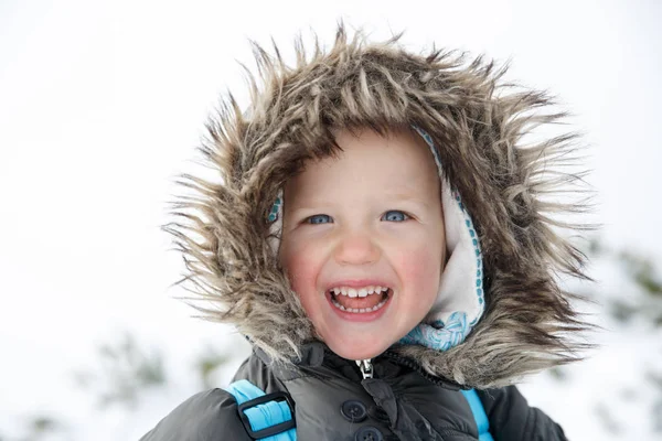 Блакитноокий маленький хлопчик в зимовому пейзажі, посміхаючись — стокове фото