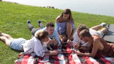 Yeşil çim ve iskambil üzerinde oturan genç insanlar göl yakınındaki.
