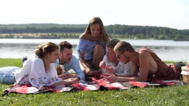 Yeşil çim ve iskambil üzerinde oturan genç insanlar göl yakınındaki.