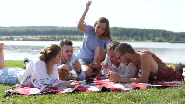 Giovani seduti sull'erba verde e giocare a carte vicino al lago . — Video Stock