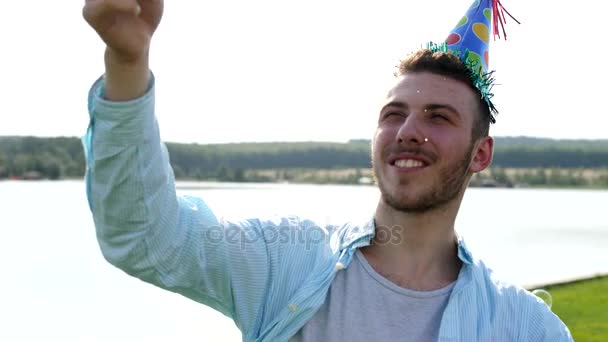 Young male blowing soap-bubbles on the lake background. — Stock Video