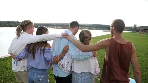 Vista trasera de un grupo de amigos disfrutando de un paseo por el lago abrazándose — Vídeos de Stock