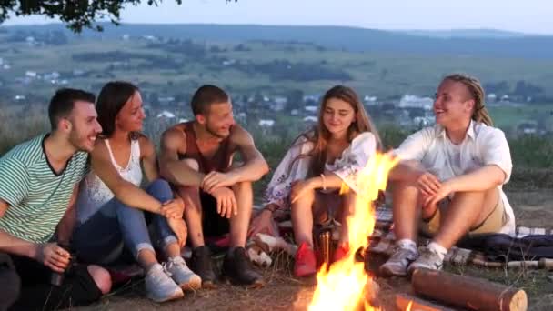 Arkadaş grubu bir kamp ateşi yanında sıcak içecekler ile oturup konuşmak — Stok video