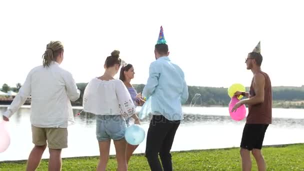 Visão traseira do grupo jovem de pessoas soprando bolhas de sabão no fundo do lago . — Vídeo de Stock