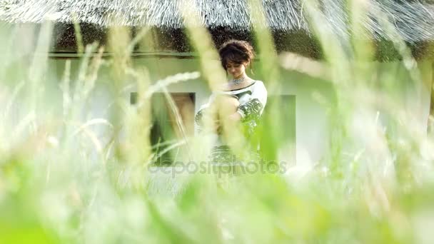 A Ukrainian girl is standing near the hut in the grass. — Stock Video