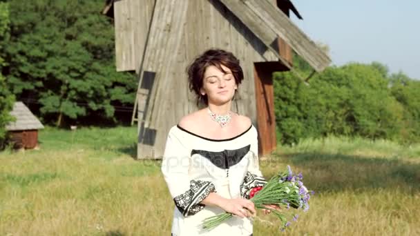 Українська дівчина ходить з квітами в лузі. — стокове відео