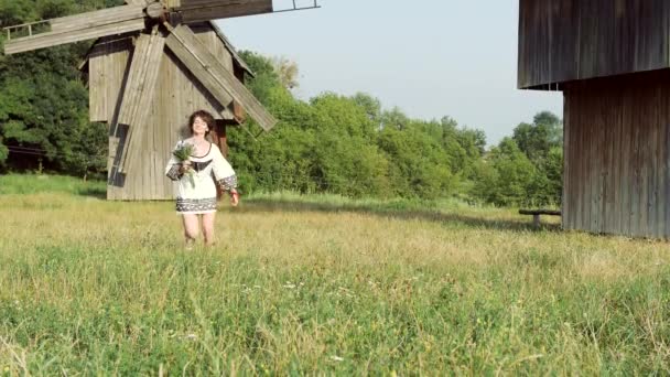 背景下，老磨房在草地上跑步的乌克兰姑娘. — 图库视频影像