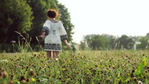 Вид сзади. Розовый клевер на фоне бегущей девушки на лугу — стоковое видео