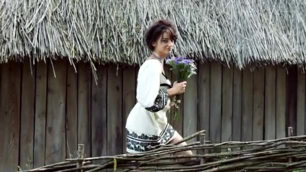 Молодая украинка проходит мимо серого сарая и смотрит в камеру . — стоковое видео