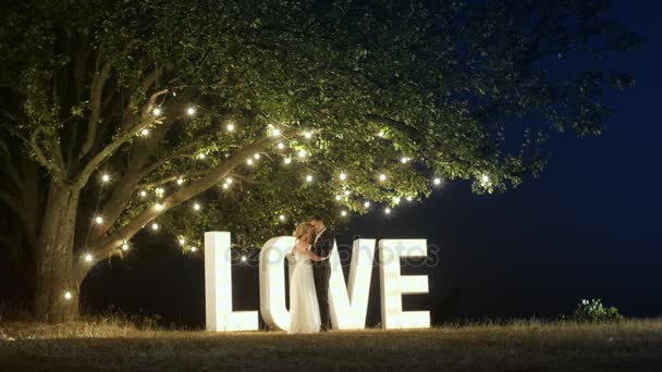Jeune couple amoureux en robes de soirée dansent près de lettres de lumière amour . — Video