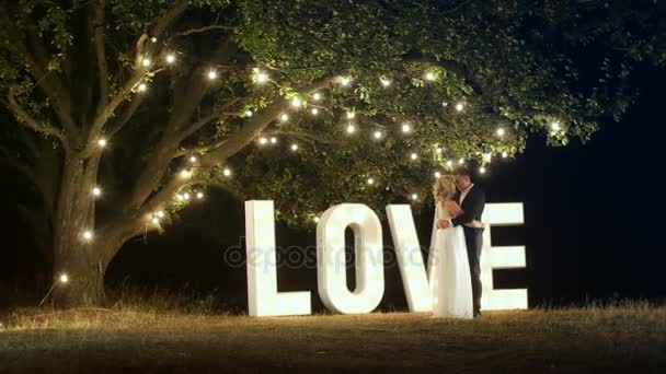 Young couple in love in evening dresses are dancing near love light letters. — Stock Video