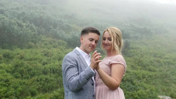 Розкішна пара в вечірніх сукнях обіймається на гірському лузі — стокове відео