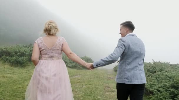 Vista trasera de la pareja corriendo en el prado de la montaña en el fondo de la niebla — Vídeos de Stock