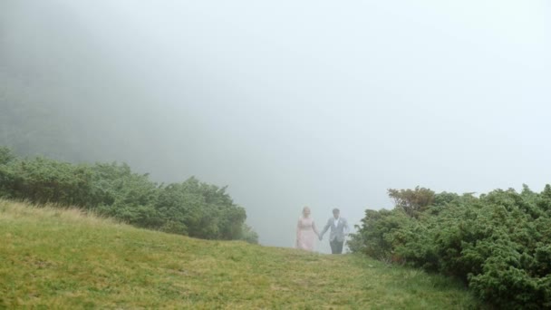 Luxury couple walking on the mountain meadow on the background of the fog — Stock Video