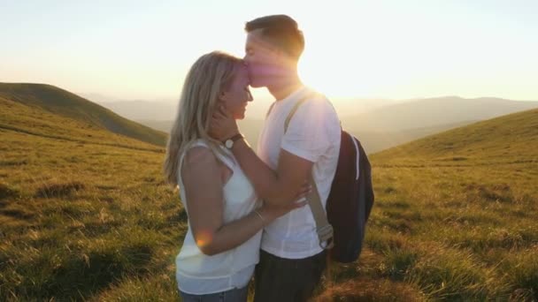 Liebendes Paar, das sich bei Sonnenuntergang auf der Wiese umarmt und küsst — Stockvideo