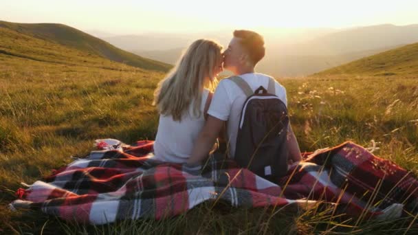Αγαπημένο ζευγάρι κάθεται σε ένα ορεινό λιβάδι και απολαμβάνει τη θέα του ηλιοβασιλέματος. — Αρχείο Βίντεο