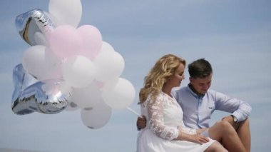 Çatıda oturan genç çift mavi gökyüzü arka planında balonlar