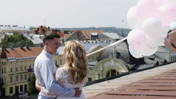 Pareja sosteniendo algunos globos en el techo abrazándose y mirando a la ciudad — Vídeos de Stock