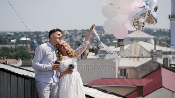 Pareja sosteniendo algunos globos y café en la azotea. — Vídeo de stock