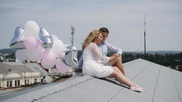 Молодая пара сидит на крыше с воздушными шарами. — стоковое видео