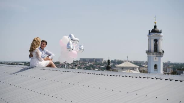 Νεαρό ζευγάρι κάθεται στην οροφή με μπαλόνια. — Αρχείο Βίντεο