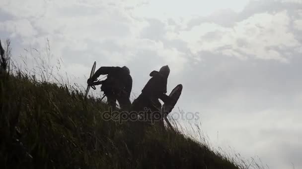 Siluetas de dos guerreros vikingos están luchando con espadas y escudos . — Vídeo de stock