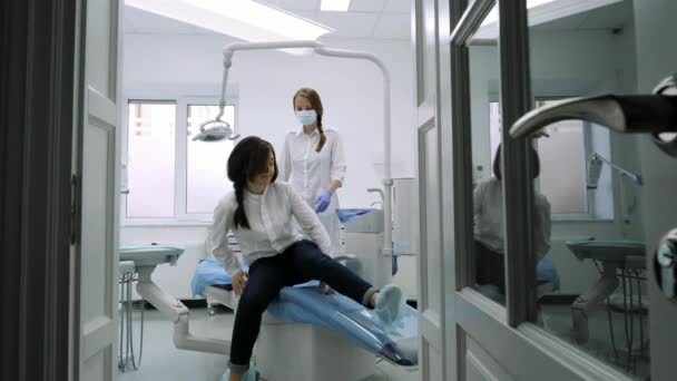 Ασθενούς που κάθεται στην καρέκλα μπλε οδοντίατρος, βοηθός οδοντίατρος βοήθεια σ ' αυτόν. — Αρχείο Βίντεο