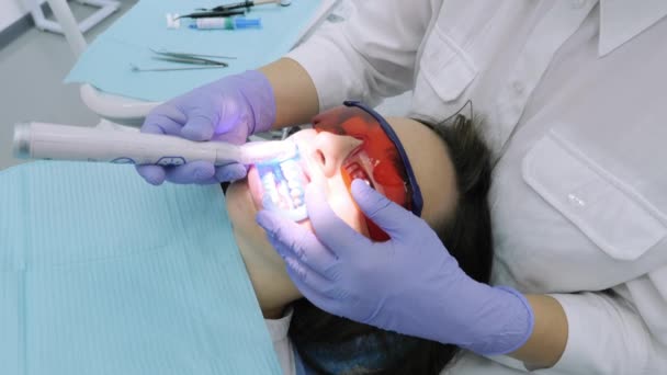 Mujer consiguiendo blanqueamiento UV en la oficina de dentistas por una máquina ultravioleta . — Vídeo de stock