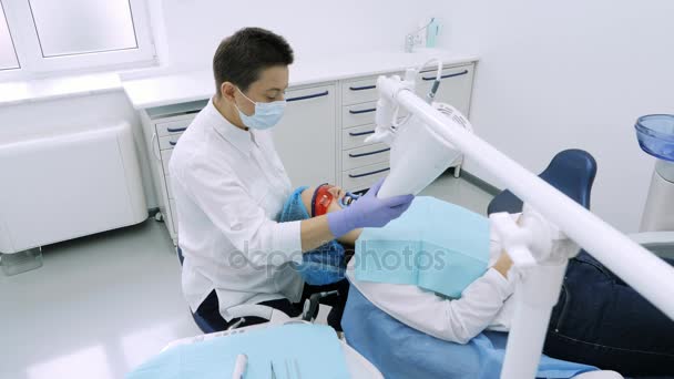 Mujer consiguiendo blanqueamiento UV en la oficina de dentistas por una máquina ultravioleta . — Vídeo de stock
