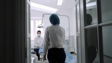 Diş hekimi hasta hasta oturur mavi diş hekimi sandalyede oturmak için davet ediyor..