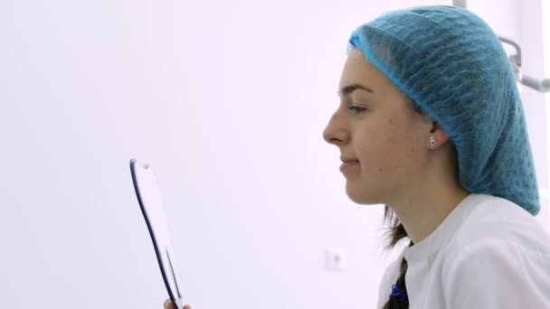 Молодая пациентка смотрит на свои зубы в зеркало в кабинете дантиста . — стоковое видео
