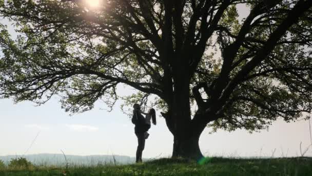 Vader houdt op handen zijn dochter en praten in de buurt van een grote boom. — Stockvideo