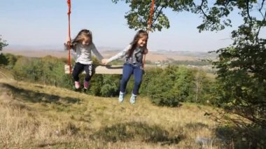 İki kız bir ağacın altında bir salıncak üzerinde sallanan.