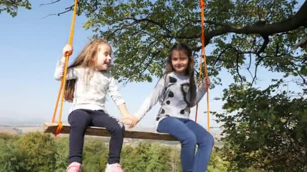 Dad shakes her daughters on a swing under a tree. — Stock Video