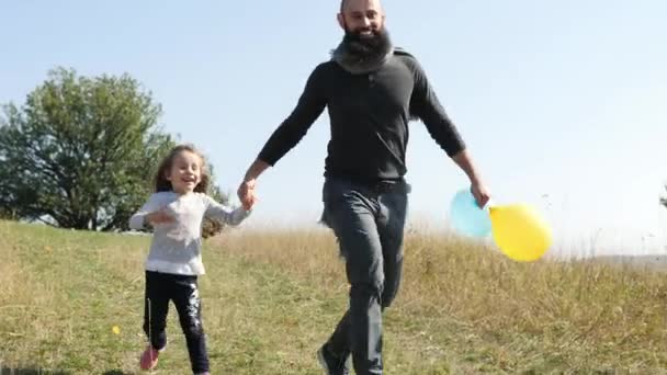 Father with his two daughters with an air balloons running down from the hill — Stock Video