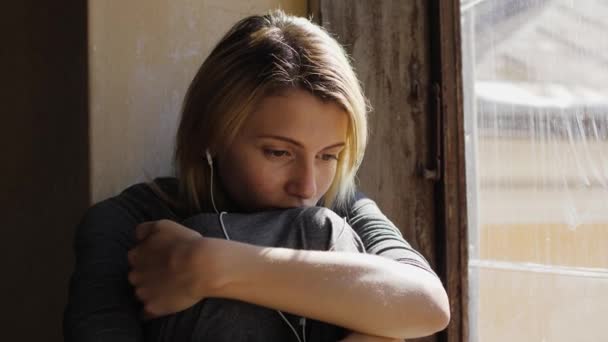 Kız pencerenin yanında kulaklıkla müzik dinlerken çok üzgün görünüyor. — Stok video