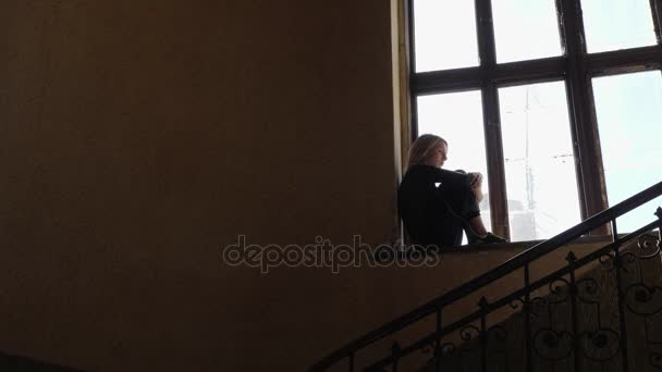Силуэт девушки выглядит грустно, слушая музыку на наушниках у окна — стоковое видео