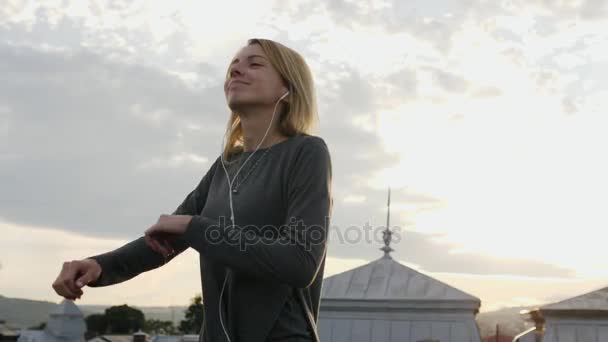 Kobieta czuje się szczęśliwy podczas słuchania muzyki w sluchawkach, taniec na dachu. — Wideo stockowe