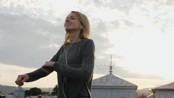 Mujer sintiéndose feliz mientras escucha música en los auriculares, bailando en la azotea . — Vídeos de Stock