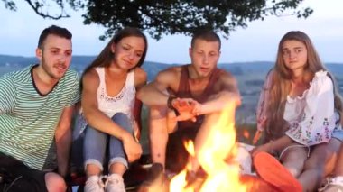 Arkadaş grubu bir kamp ateşi yanında sıcak içecekler ile oturup konuşmak
