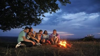 Arkadaş grubu bir kamp ateşi yanında sıcak içecekler ile oturup konuşmak