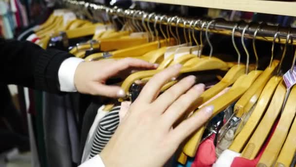 Primer plano de las manos de las mujeres corren a través de un estante de ropa, navegar en una boutique . — Vídeo de stock