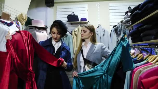 Dos novias sonrientes eligen la ropa en la tienda . — Vídeo de stock