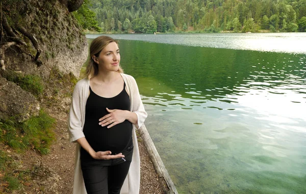 Vacker gravid kvinna nära en fjällsjö i skogen. — Stockfoto