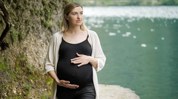 Vacker gravid kvinna nära en fjällsjö i skogen. — Stockfoto