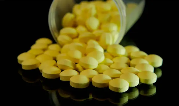 Yellow pills scattered from a transparent bottle are scattered on a glass black table — Stock Photo, Image