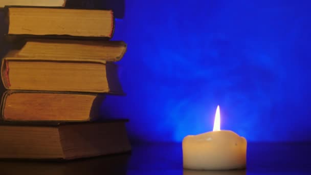 Hromádky knih stojí u hořící svíčky a barevný kouzelný kouř létá. — Stock video