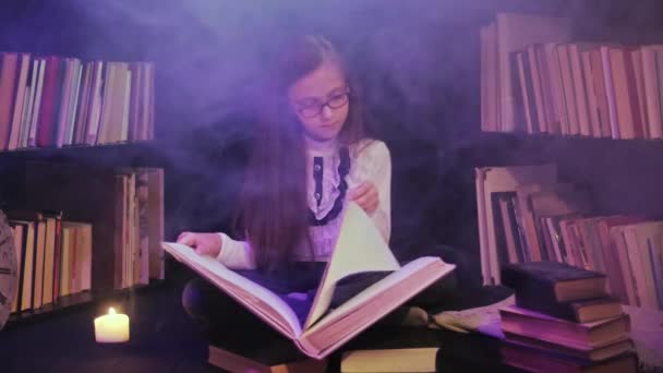 Dívka otevře pohádkovou knížku v knihovně, barevný kouř se točí dokola, svíčky jsou zapálené poblíž — Stock video