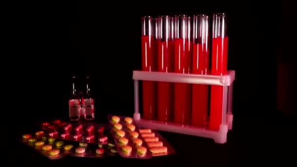 Pastillas sobre fondo de tubos de ensayo con líquido rojo sobre fondo negro — Vídeo de stock